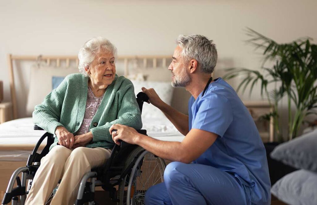 Caregiver helping an older resident sanitize hands in a clean assisted living common area.
